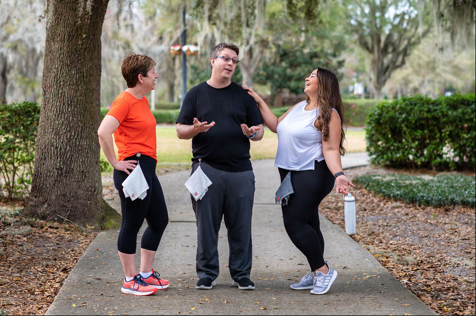 Three people standing on a sidewalk in a park-like setting wearing Dry in Stride towels.