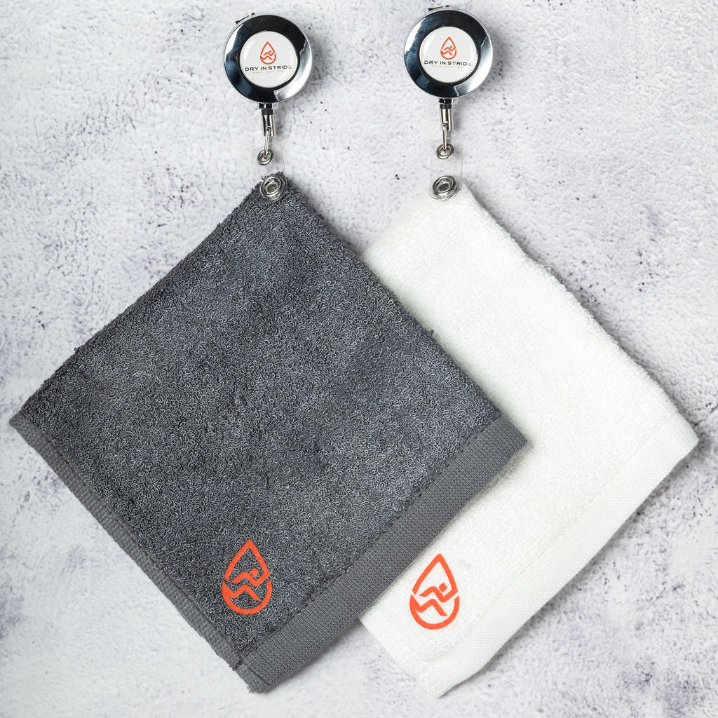 Two Dry in Stride towels, with clips.  One is gray and one is white on a textured surface.