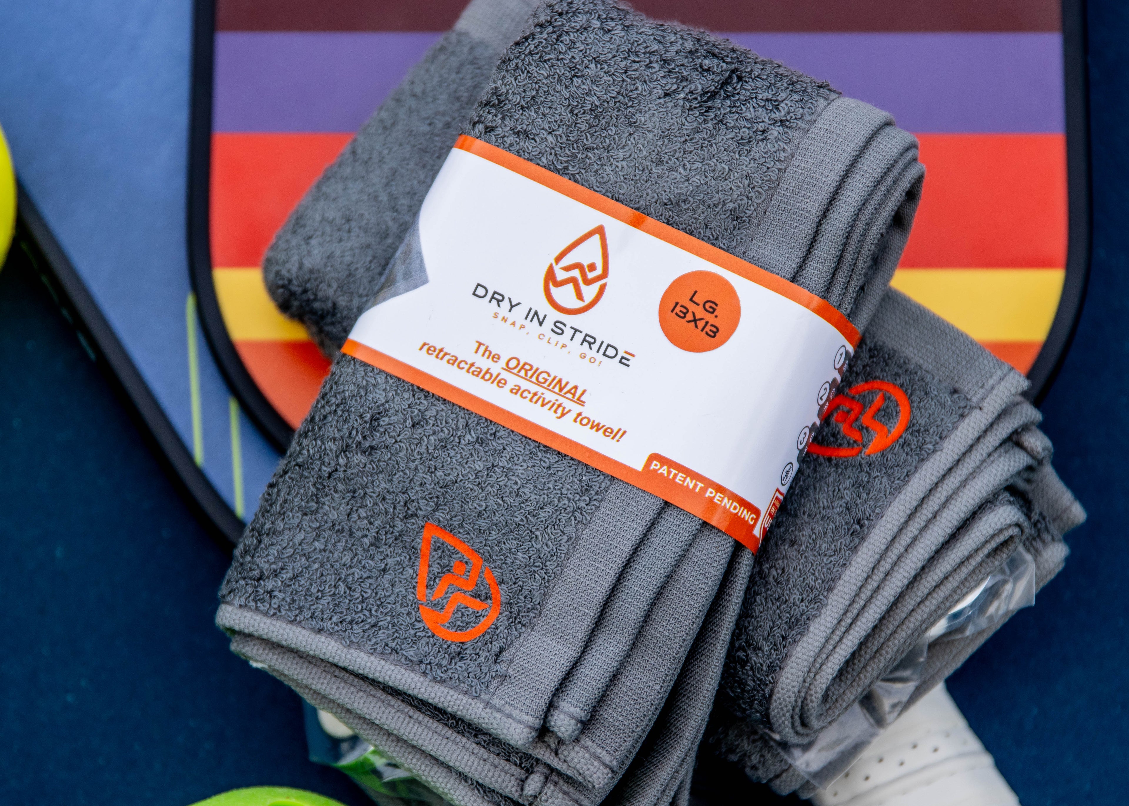 Pair of Dry in Stride towel sets on a colorful pickleball paddle background