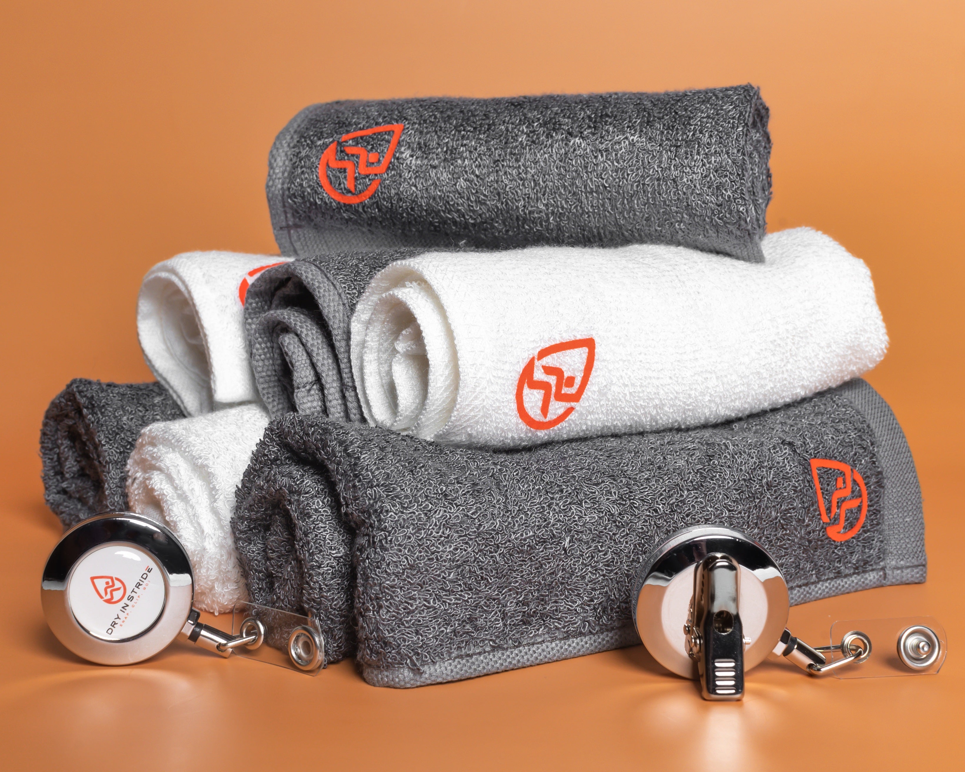 Stack of rolled Dry in Stride gray and white towels with clips on an orange background
